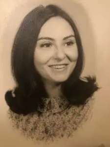 Black and white portrait of a smiling woman with long hair wearing a patterned top; suitable for funeral services, cremations, or pre-planning imagery.