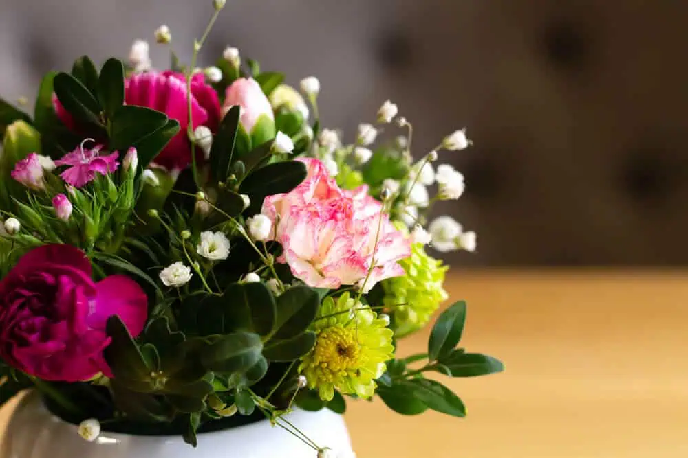 A bouquet of vibrant pink and green flowers with lush greenery in a white vase on a wooden surface, reflecting serene beauty; ideal for green burial services in Alabama.